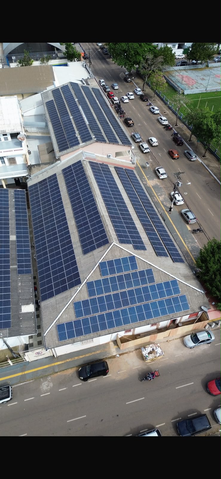 Vista aérea de telhado comercial coberto por painéis solares, em área urbana